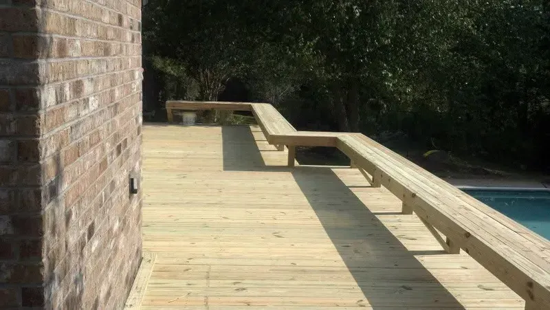 Wooden deck with a built-in bench next to a brick wall and pool.