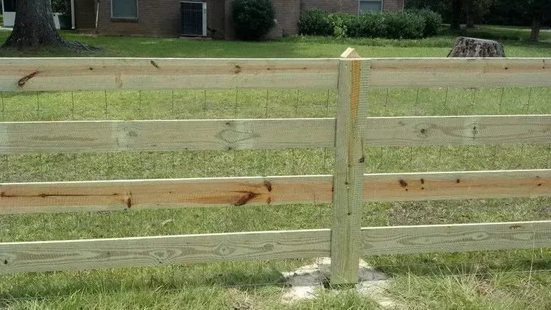 Wooden split-rail fence in a grassy yard, with a home and trees in the background.
