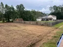 Cleared land with a house and a wooden fence in the background, under a cloudy sky.