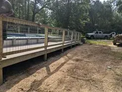 Wooden deck with wire fencing overlooks a pool; a truck and woods are in the background.