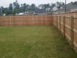 A wooden fence encloses a green lawn, houses in the background.