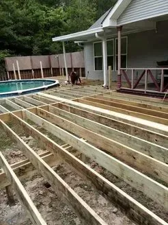 Deck under construction next to a pool and house; a person works on the framing.