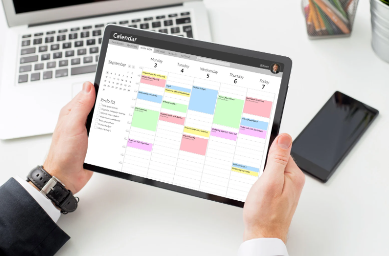 A person is holding a tablet with a calendar on it.