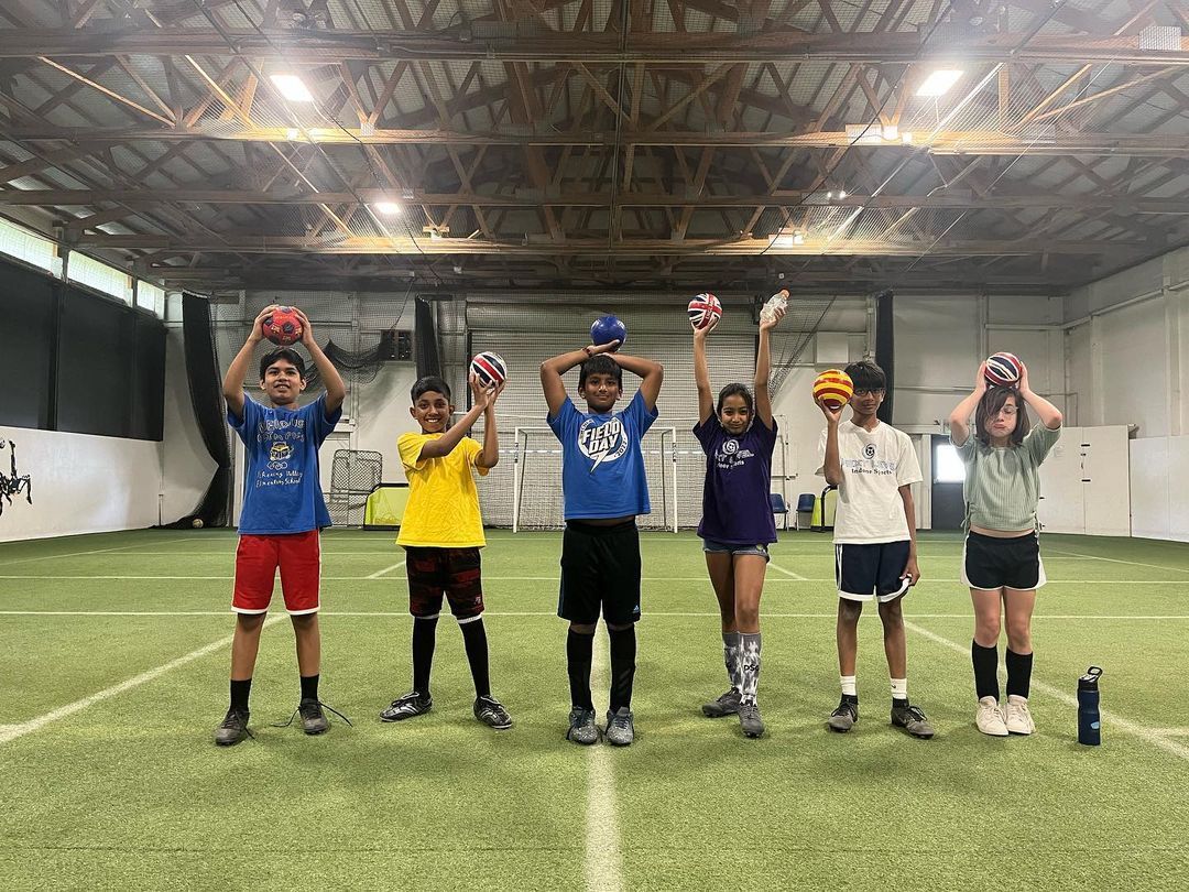 A group of children are standing on a soccer field holding soccer balls over their heads.