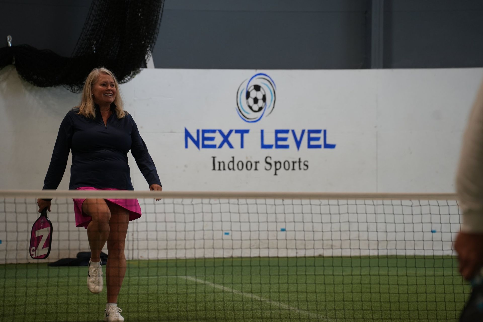 A woman is playing tennis in front of a sign that says next level indoor sports