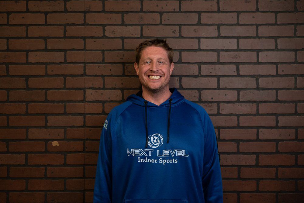 A man wearing a blue hoodie is standing in front of a brick wall.