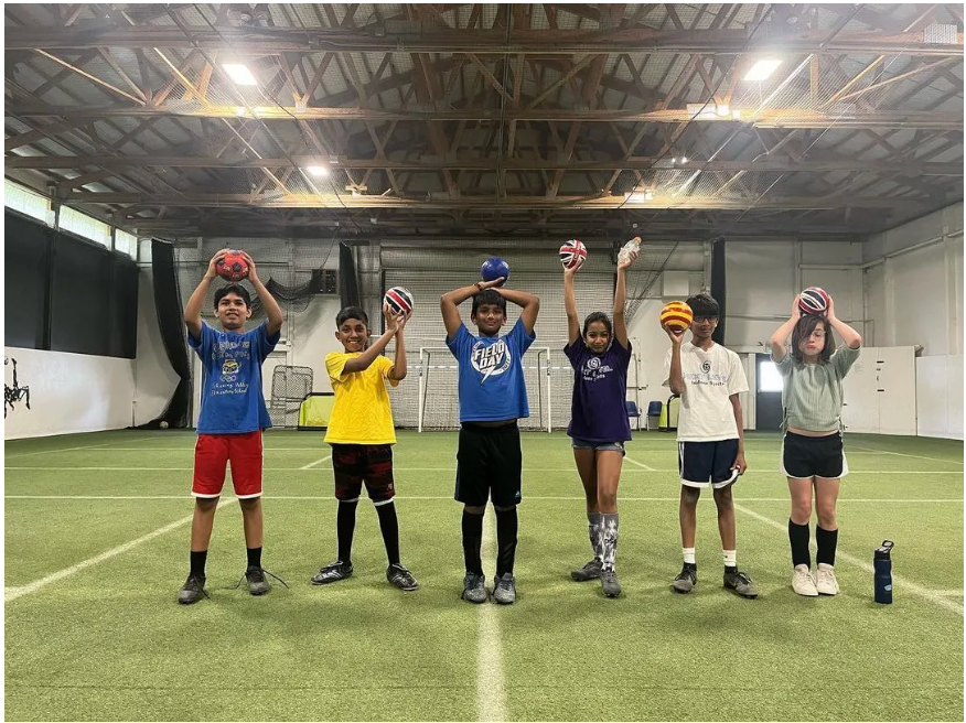 A group of children are standing on a soccer field holding soccer balls over their heads.