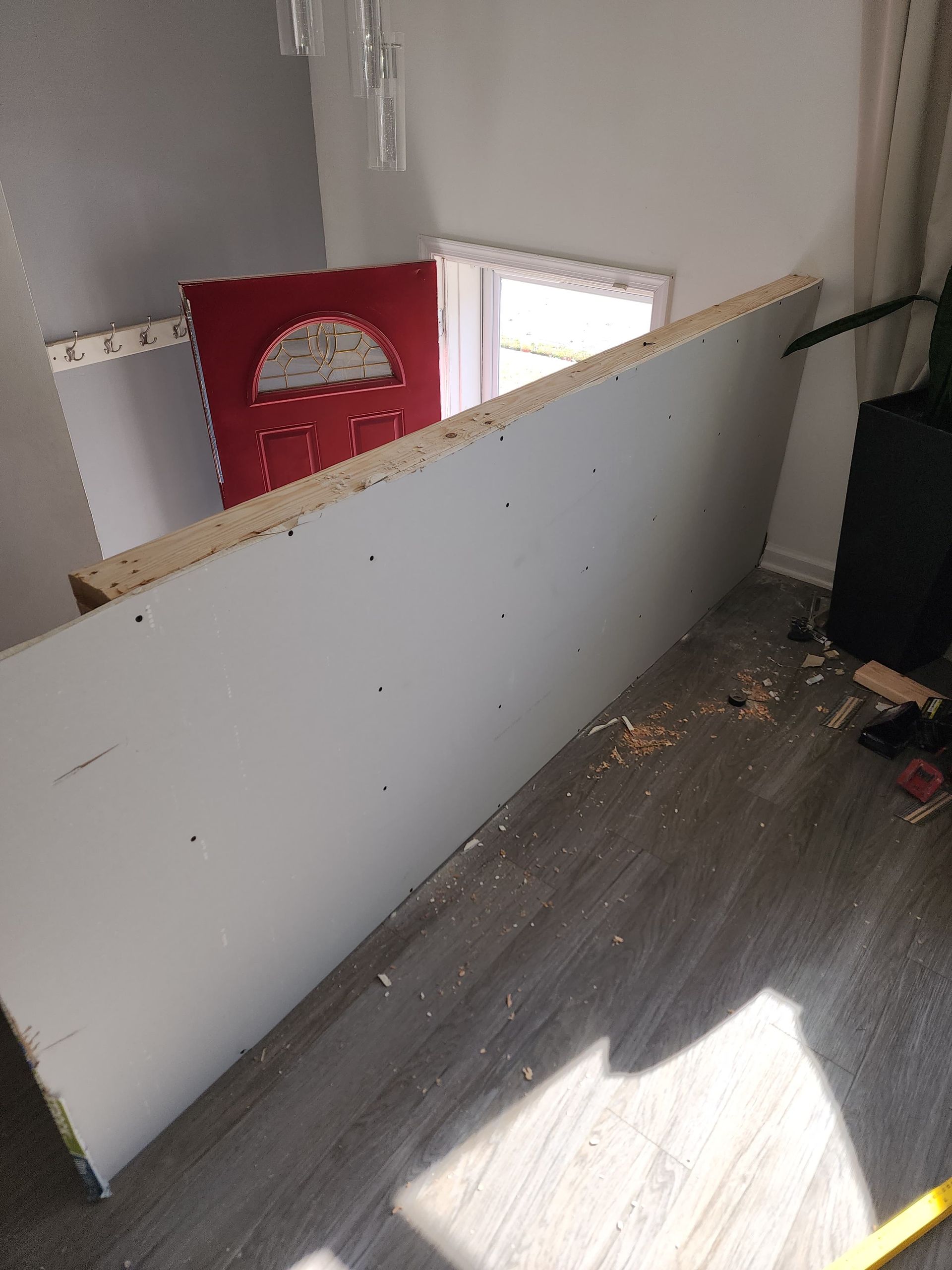 White wall, likely a partition, on a wood floor near a red door and a window.