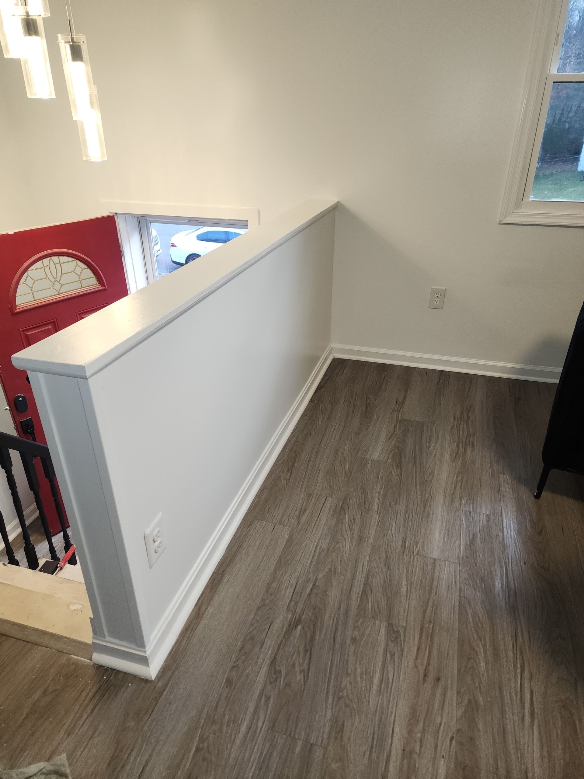 White-walled interior with a half-wall, wood-look flooring, and a red door visible in the background.