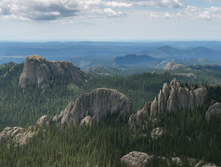 Rocky mountain peaks rise above a dense forest under a cloudy sky.