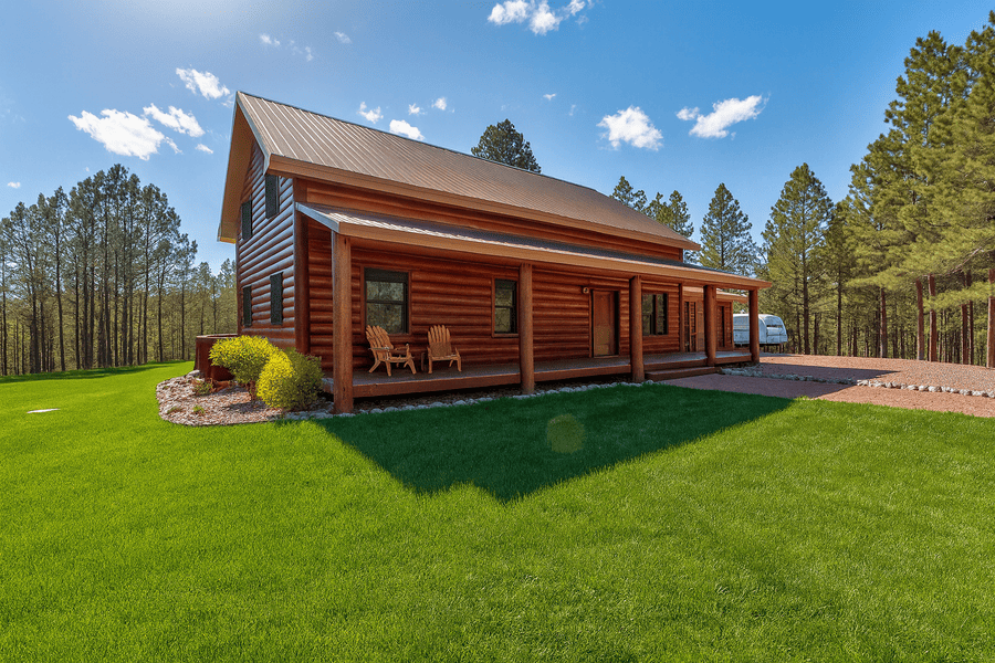 Hermosa Log cabin with a porch on a green lawn with trees in the background under a blue sky.