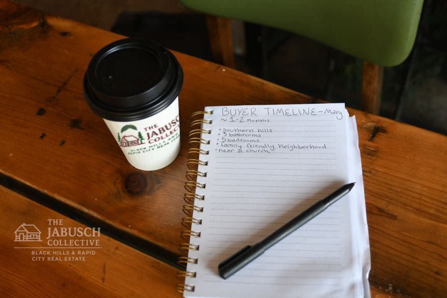 A cup of coffee and a notebook with a pen on a wooden table.