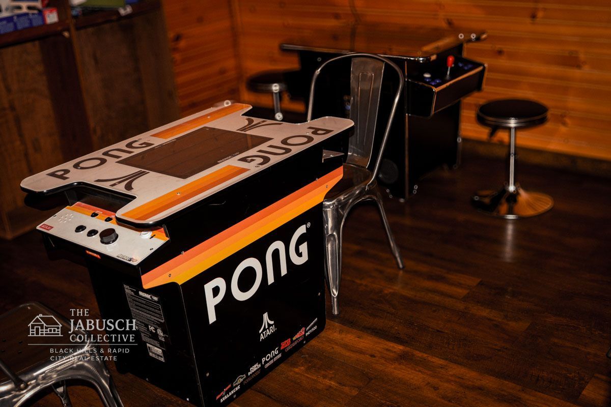 Pong arcade table at the Prairie Dog Taproom with metal chairs, wooden paneling, and a black arcade cabinet in a game room.