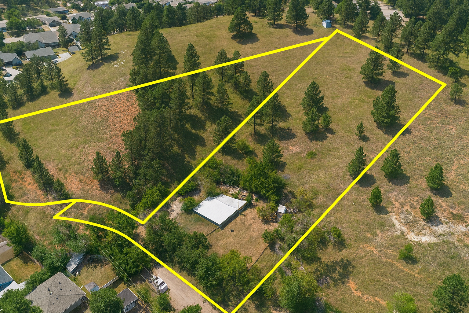 Aerial view of a plot of land with a house, outlined in yellow; trees and dry grass.