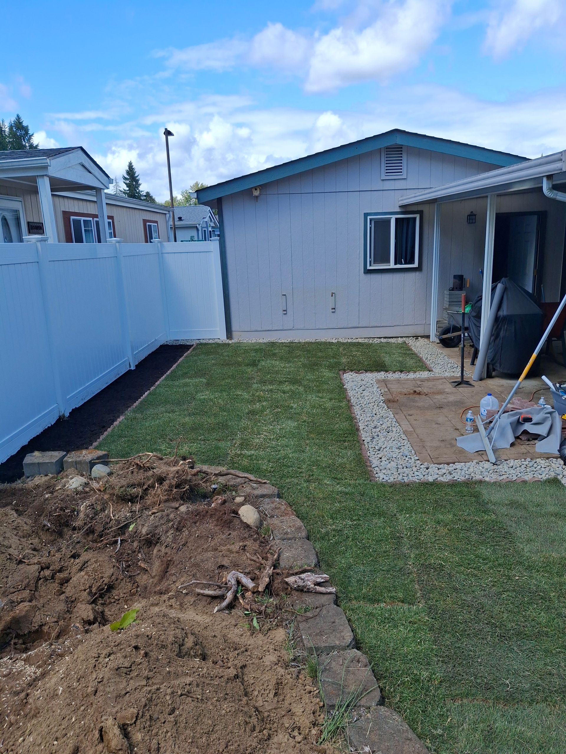 Backyard with freshly tilled soil, a stone border, wooden fence, and shovel.