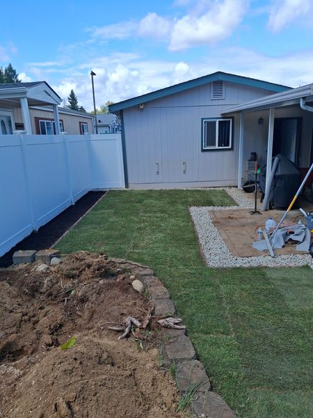 A backyard with a white fence and a house in the background.