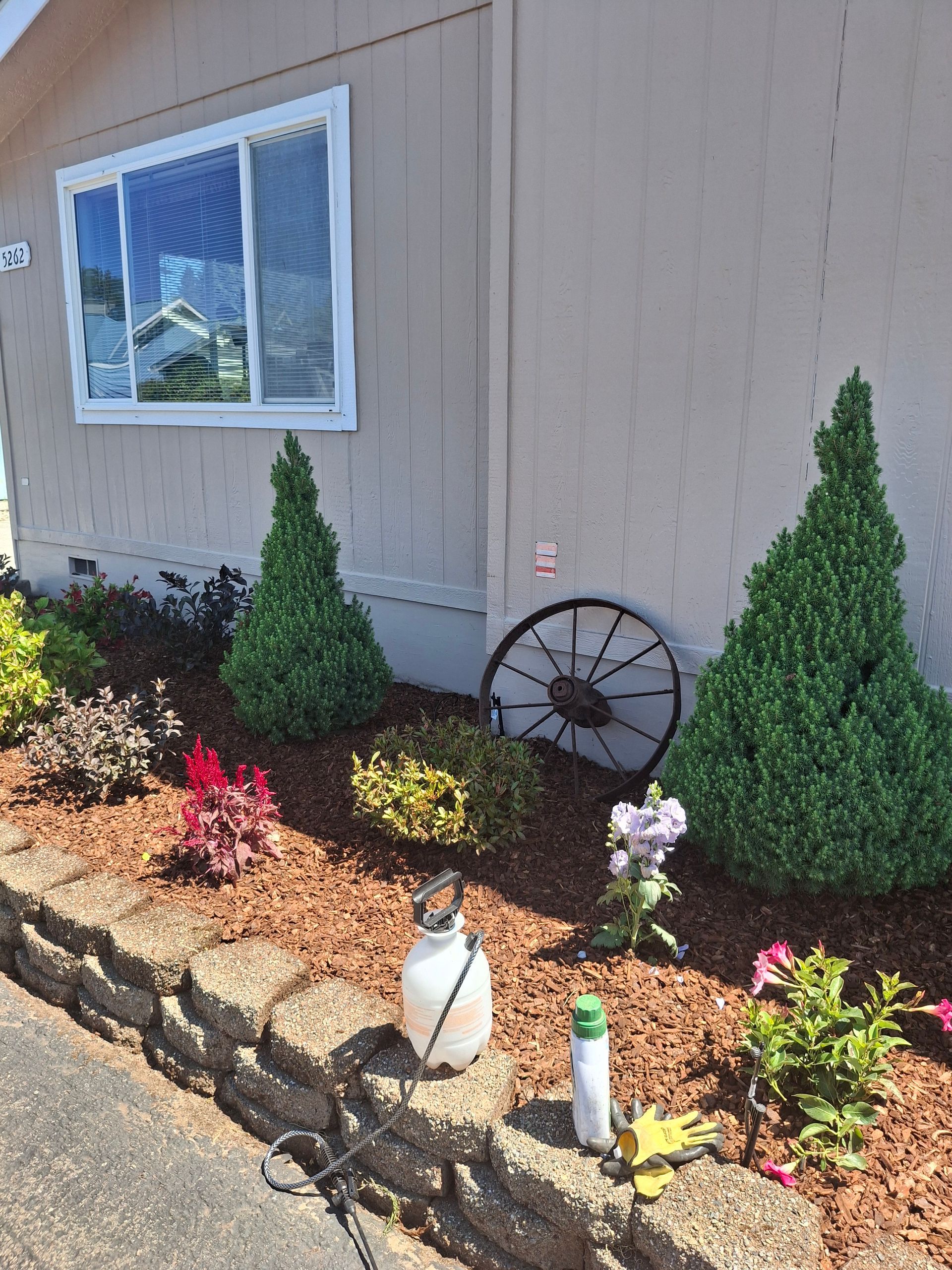 A house with a garden in front of it and a wagon wheel.