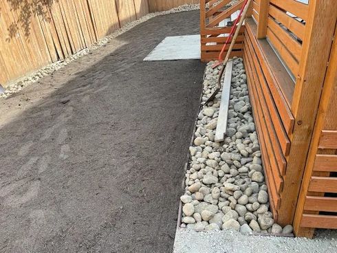 A narrow gravel pathway alongside a wooden fence, with a rock border.