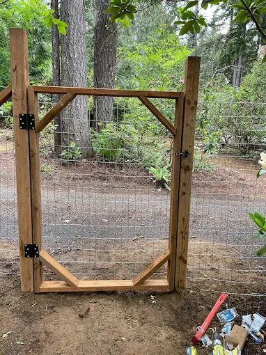 Wooden gate with wire mesh, surrounded by trees and a dirt path.