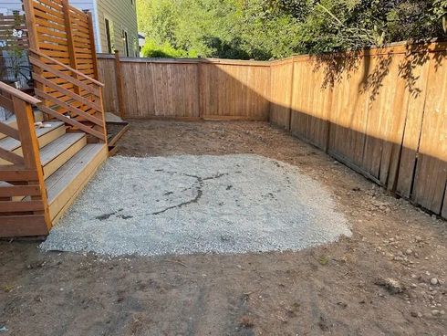 A gravel base for a patio in a fenced backyard, next to a wooden deck.