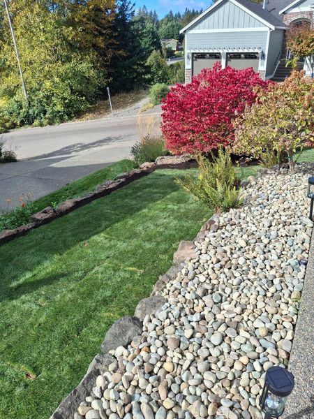 Well-manicured front yard with stone border, lush green lawn, and autumn foliage, with a house in the background.
