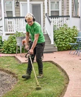 A man wearing headphones is using a lawn mower to cut the grass.
