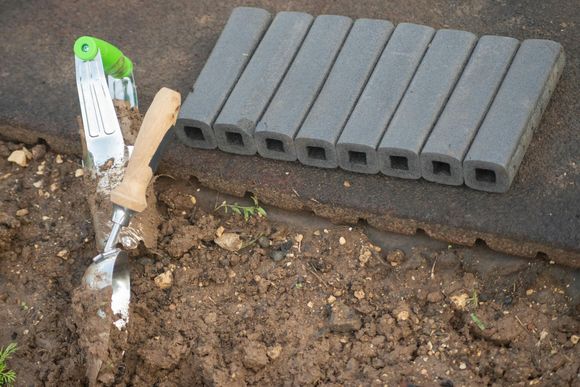 A shovel is in the dirt next to a pile of bricks