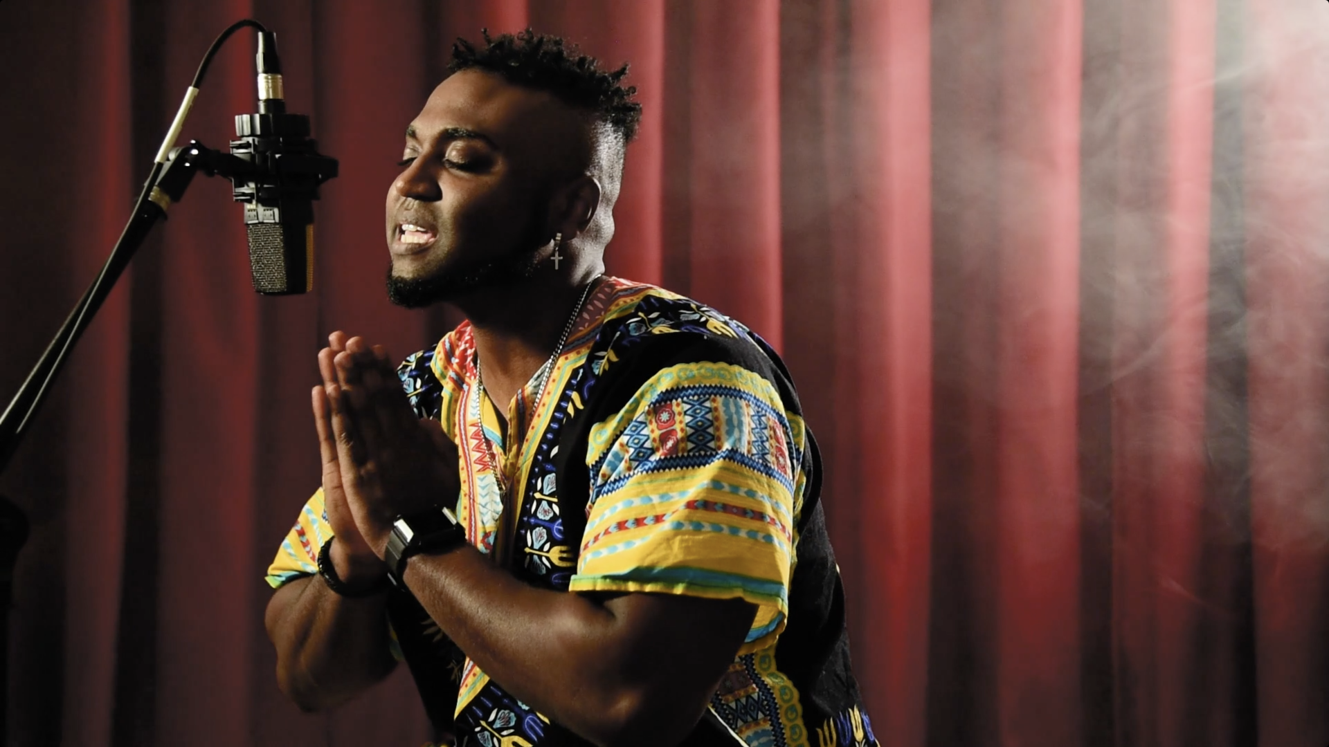 A man is singing into a microphone in front of a red curtain.