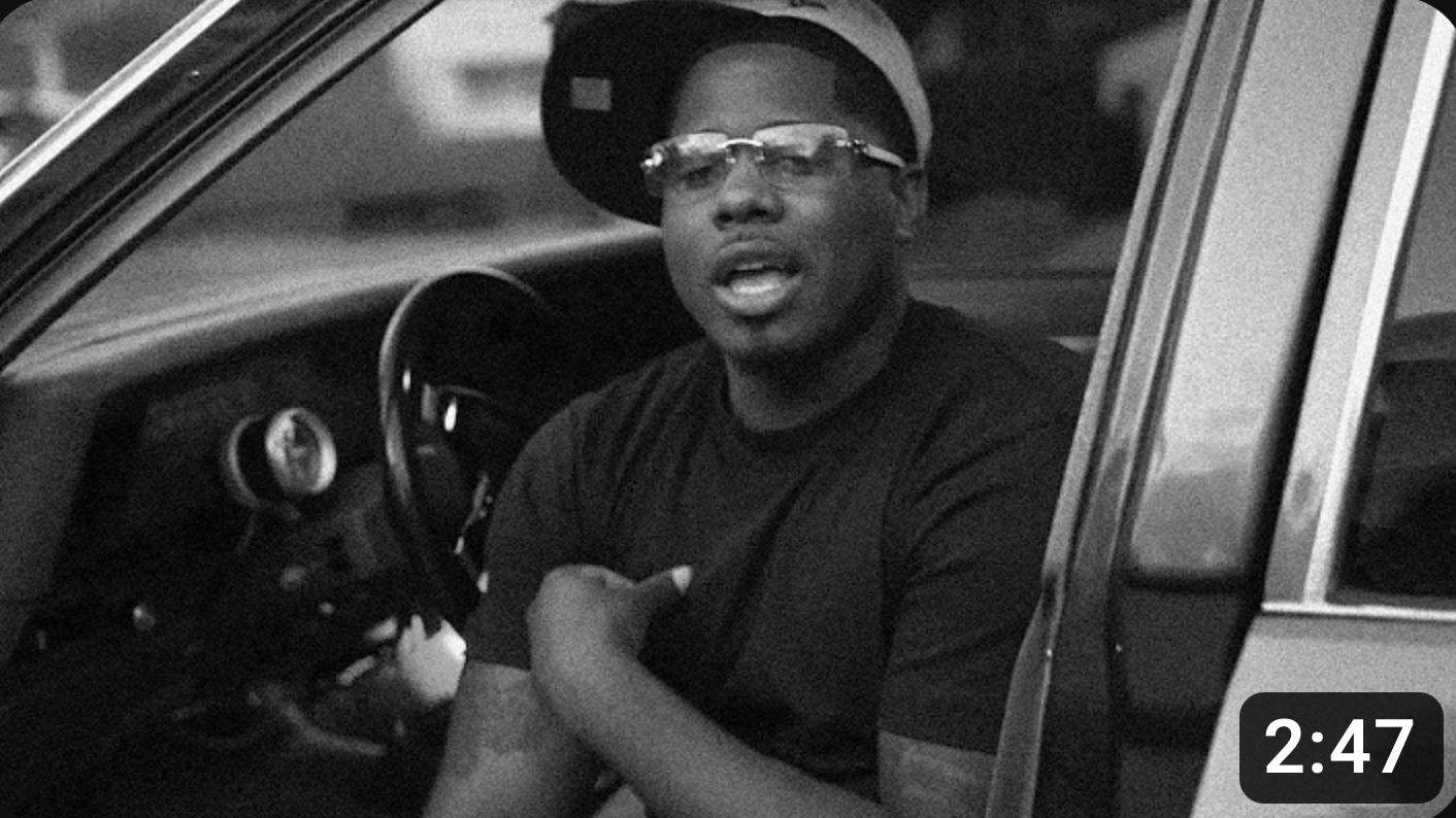 A black and white photo of a man sitting in a car.