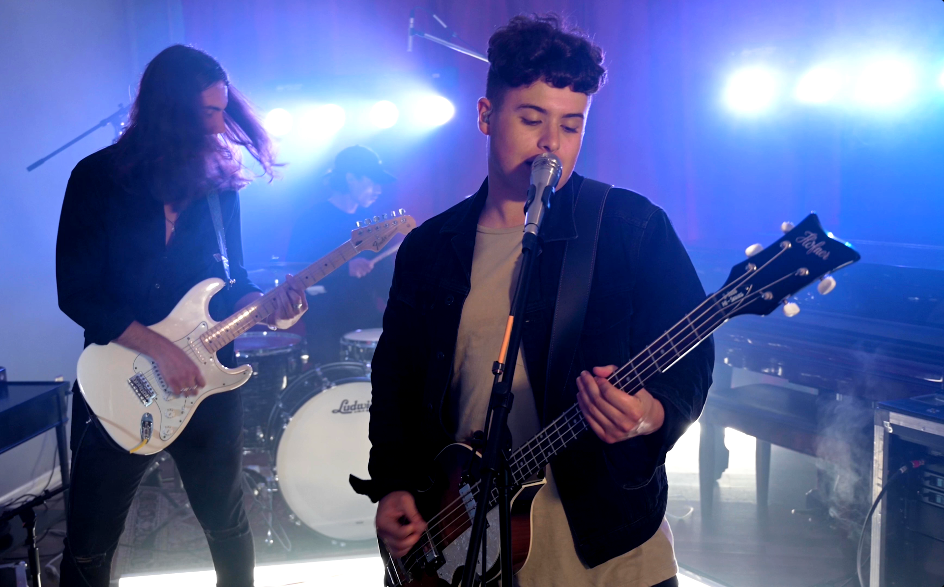 A woman is singing into a microphone while playing a guitar in a band.