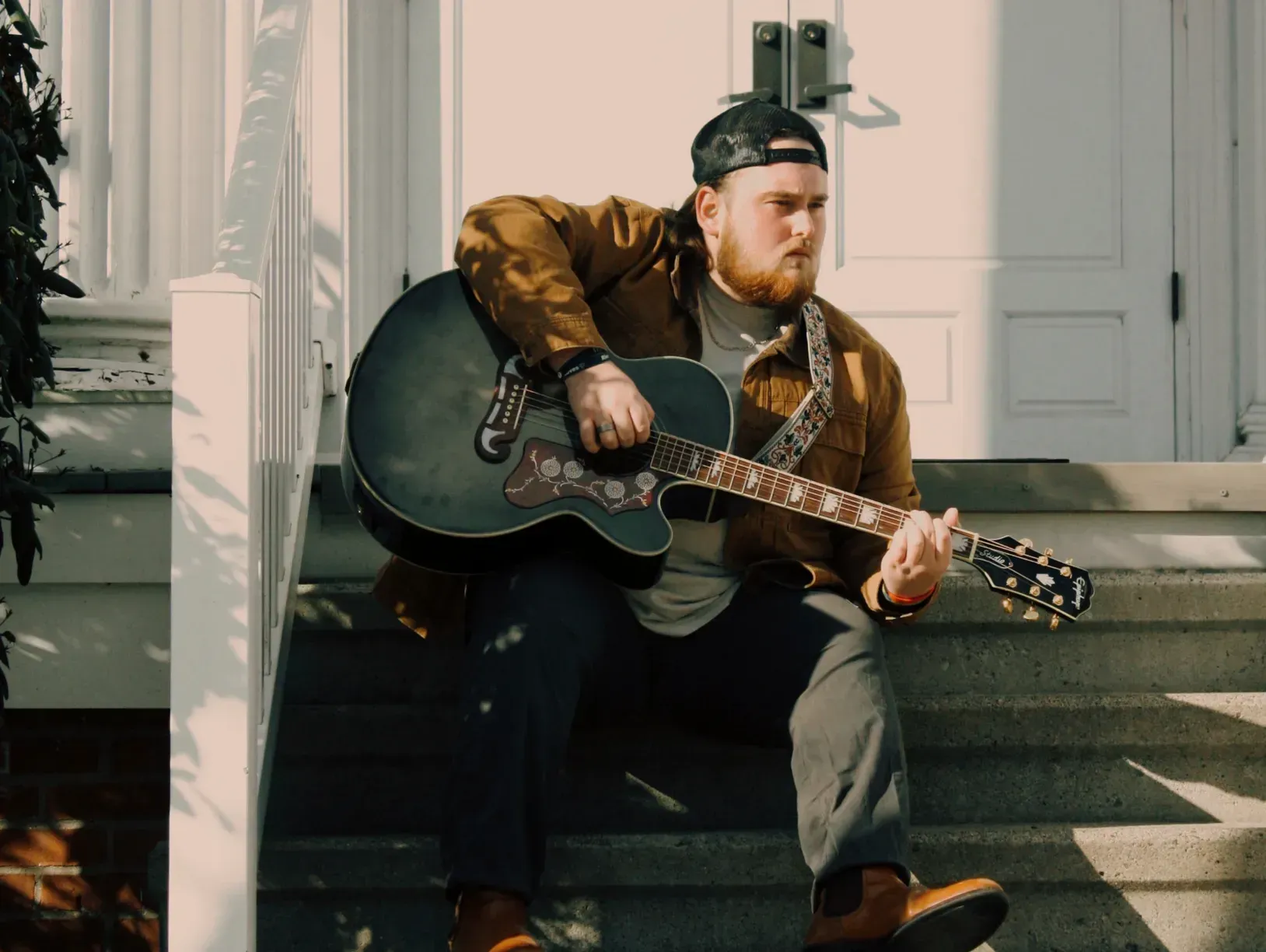 A man is sitting on the steps of a building playing a guitar.