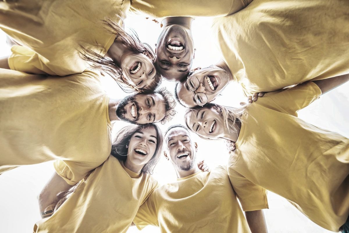 Un gruppo di persone è in piedi in cerchio e guarda la telecamera dall'alto in basso.
