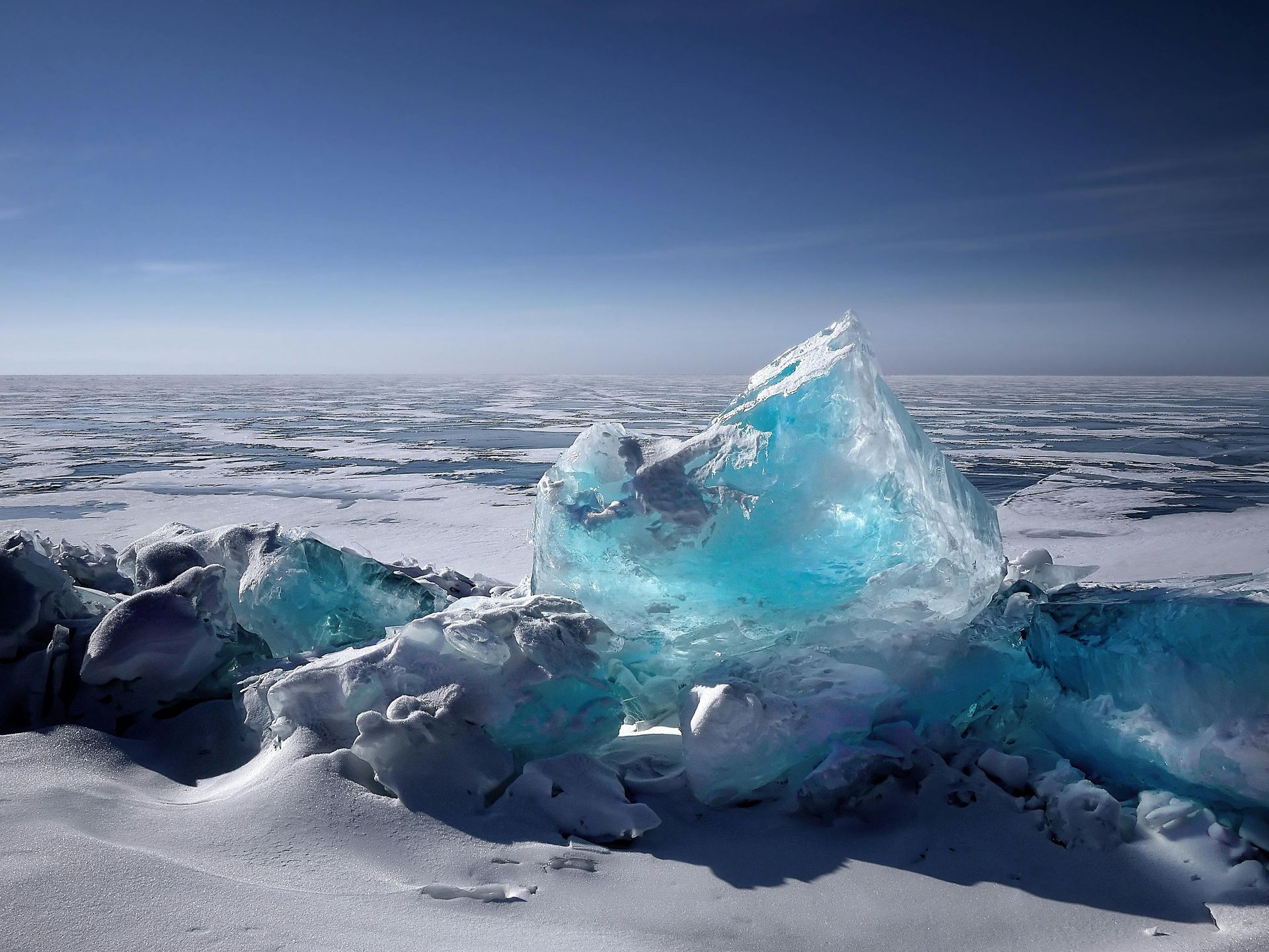 Un grande pezzo di ghiaccio blu si trova in mezzo a un campo innevato.