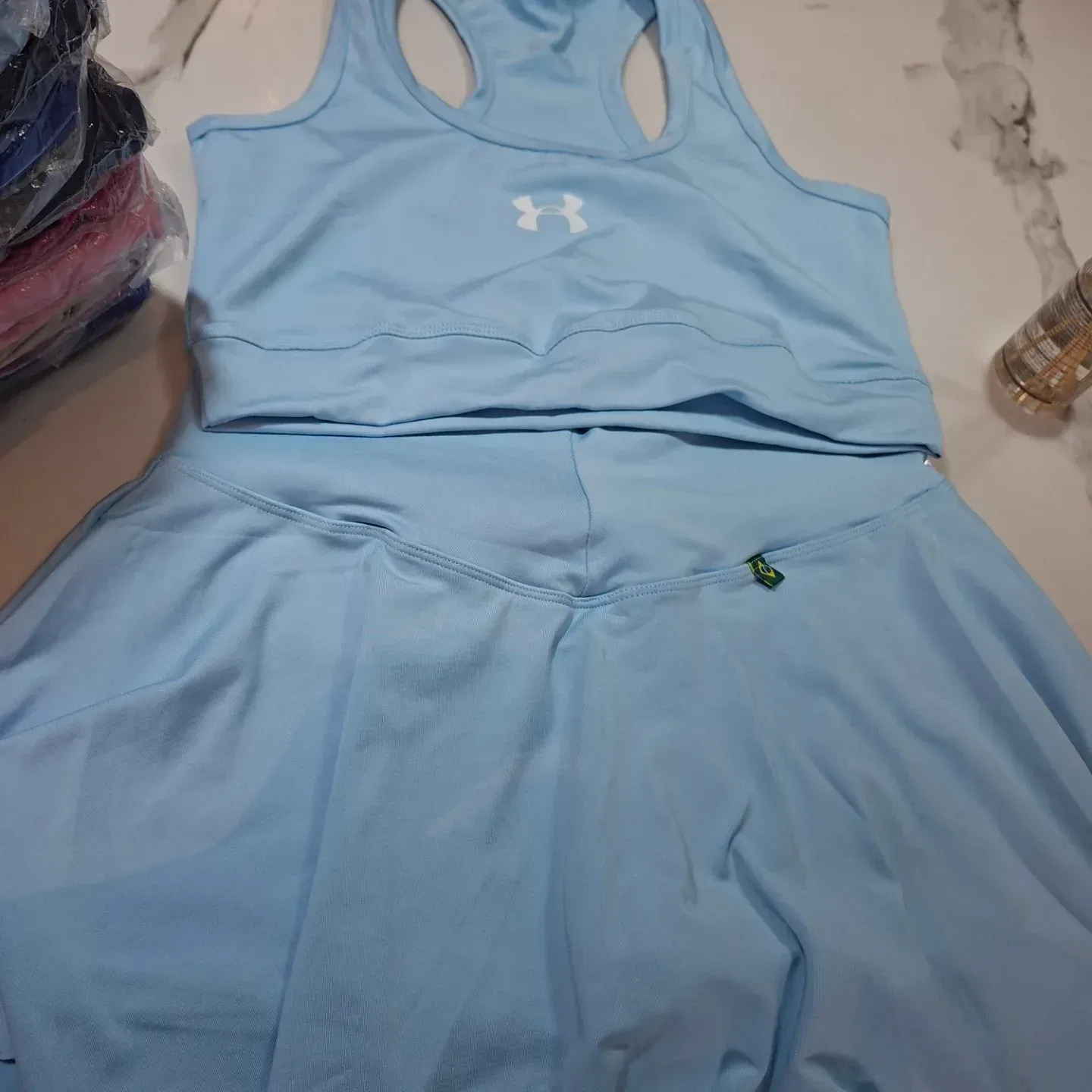 Conjunto deportivo azul claro: top corto y falda. Logotipo de Under Armour visible.