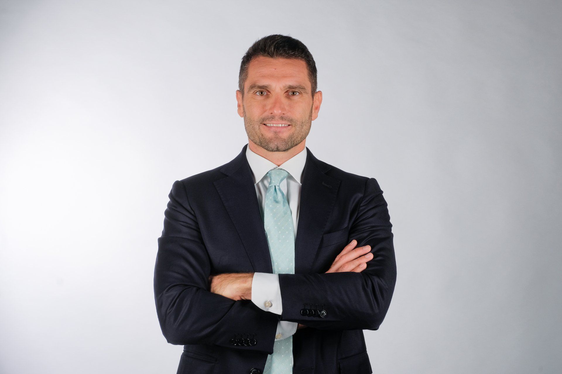 Un uomo in giacca e cravatta è in piedi con le braccia incrociate.