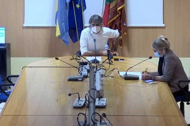 Un uomo e una donna sono seduti a un lungo tavolo con dei microfoni.