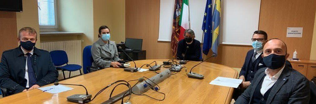 Un gruppo di persone che indossano maschere sono seduti attorno a un tavolo da conferenza.