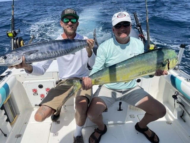 Two men are sitting on a boat holding large fish.