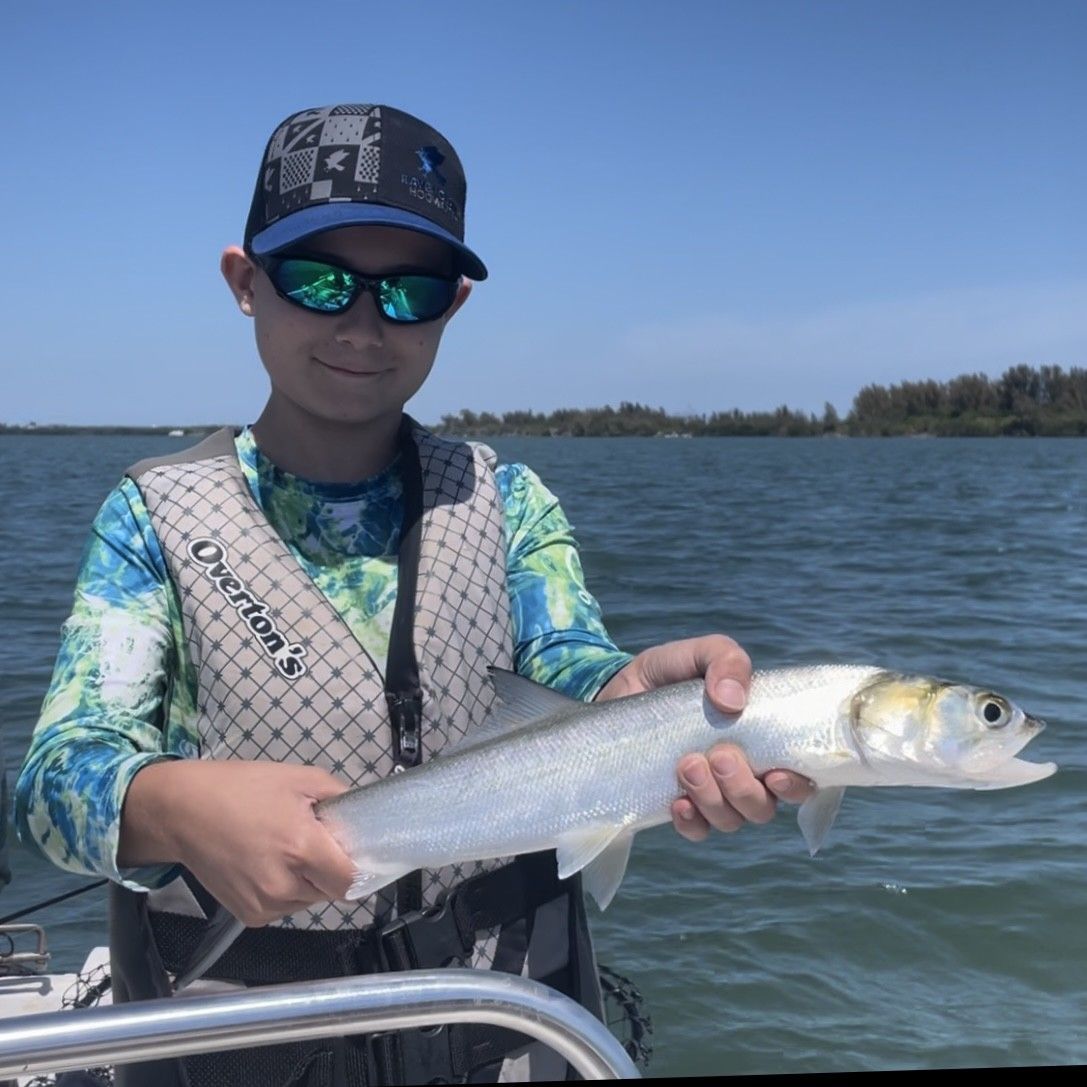 A young boy holding a fish on a boat with a vest that says overlook on it