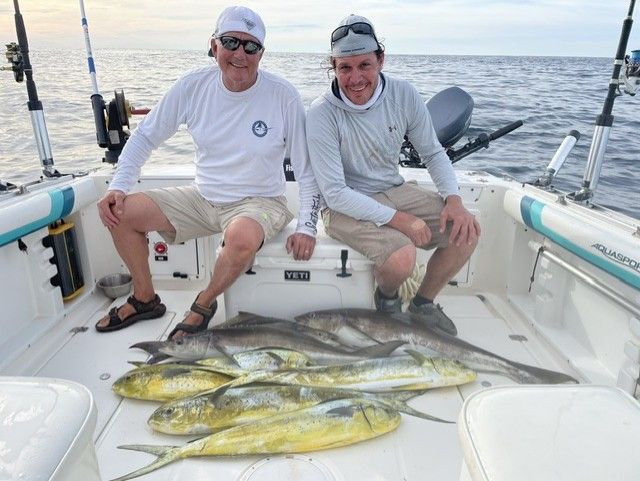 Two men are sitting on a boat with a bunch of fish on the deck.