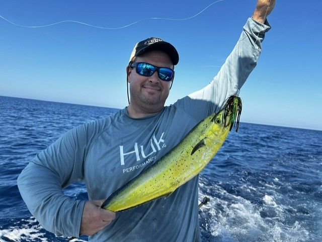 A man in a huk shirt is holding a fish over his head
