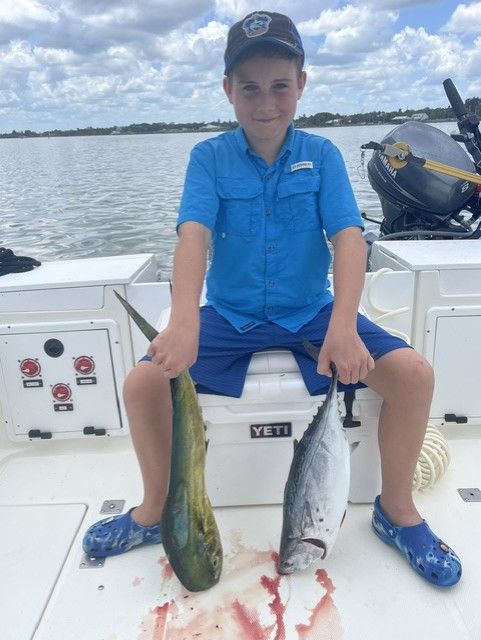 A young boy is sitting on a boat holding two fish