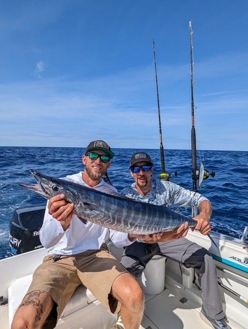 Two men are sitting on a boat holding a large fish.