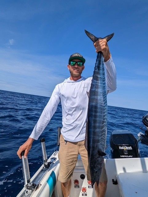 A man is holding a large fish on a boat in the ocean.