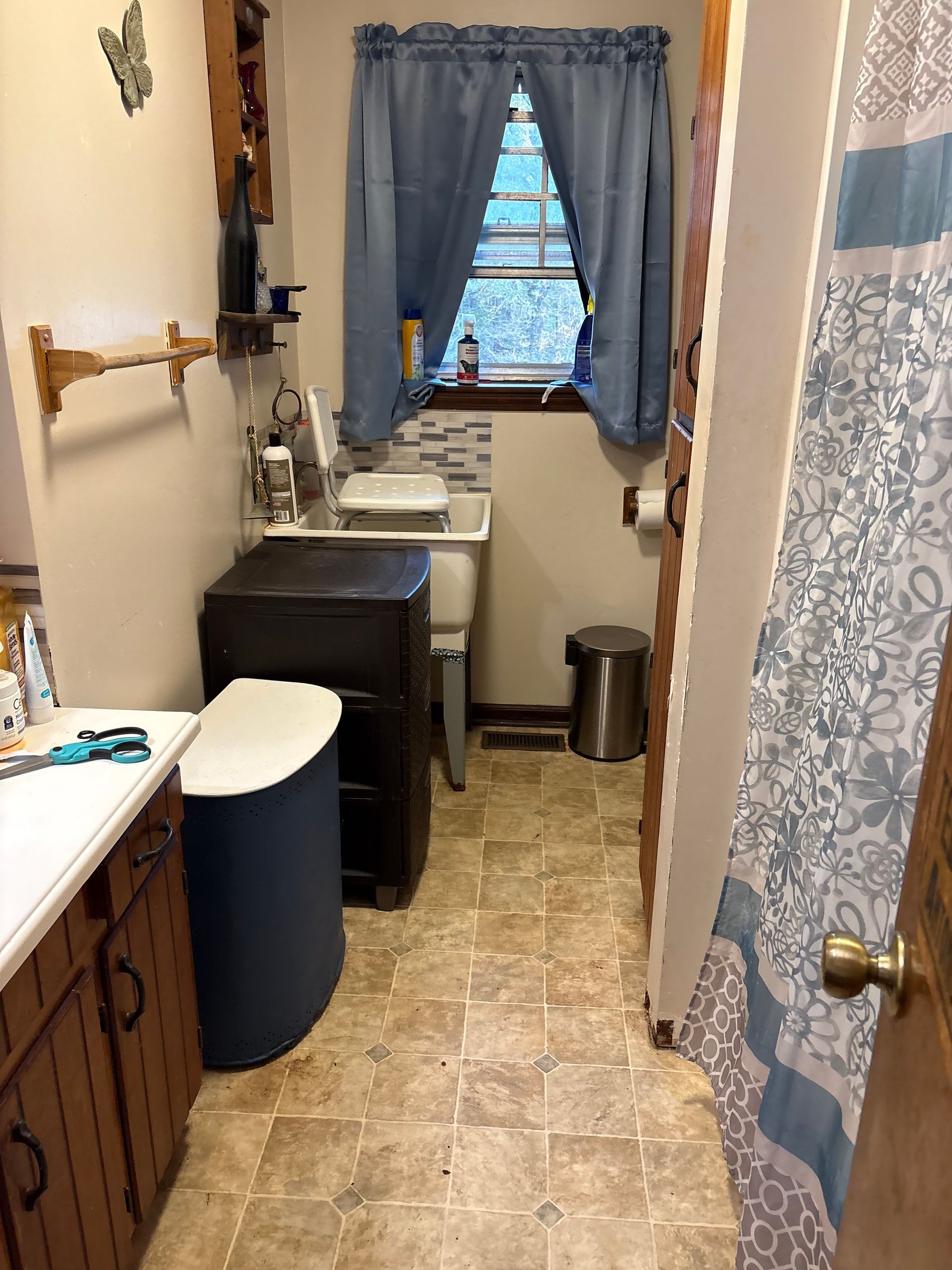 Small bathroom with toilet, sink, and shower curtain; blue curtains over window.