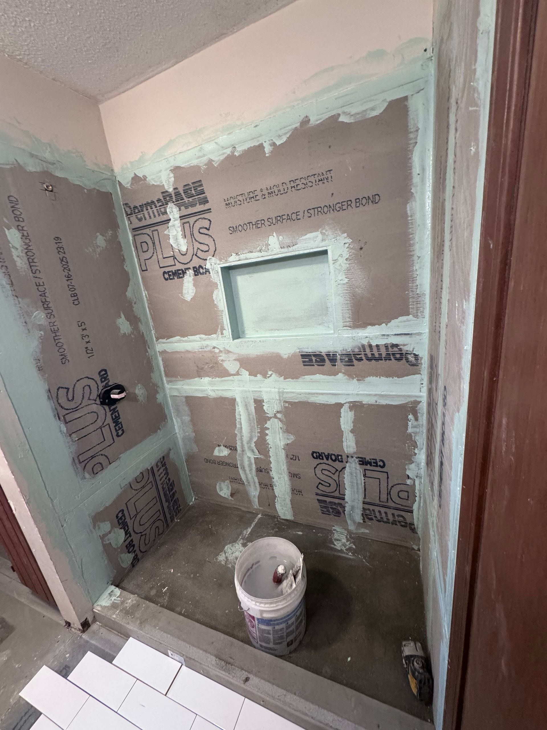 Shower construction: Cement board walls, niche, bucket on floor, green sealant visible.