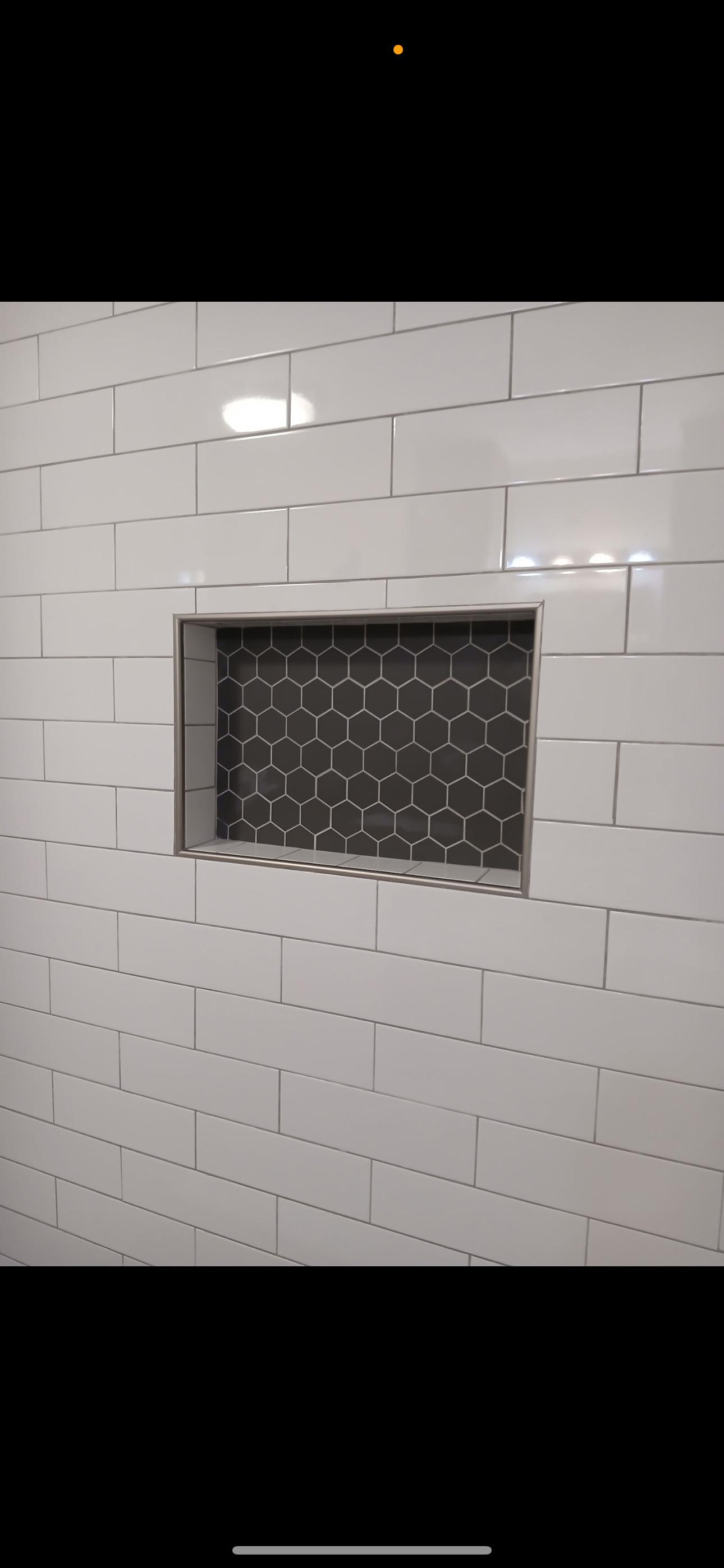 White tile wall with recessed shelf lined with black hexagon tiles.