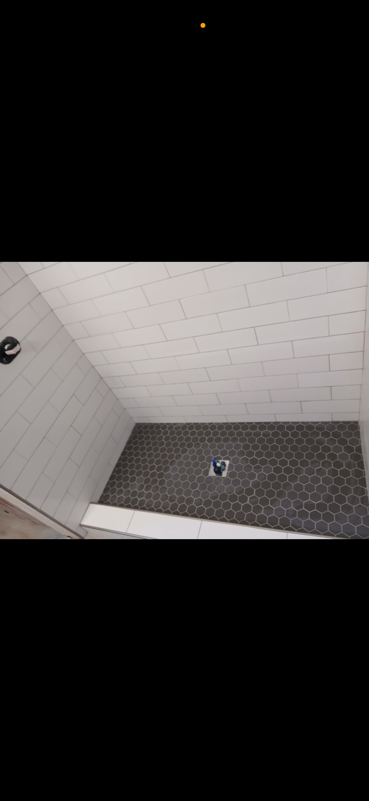 Shower stall with dark floor tiles and white wall tiles. A drain sits in the center of the floor.