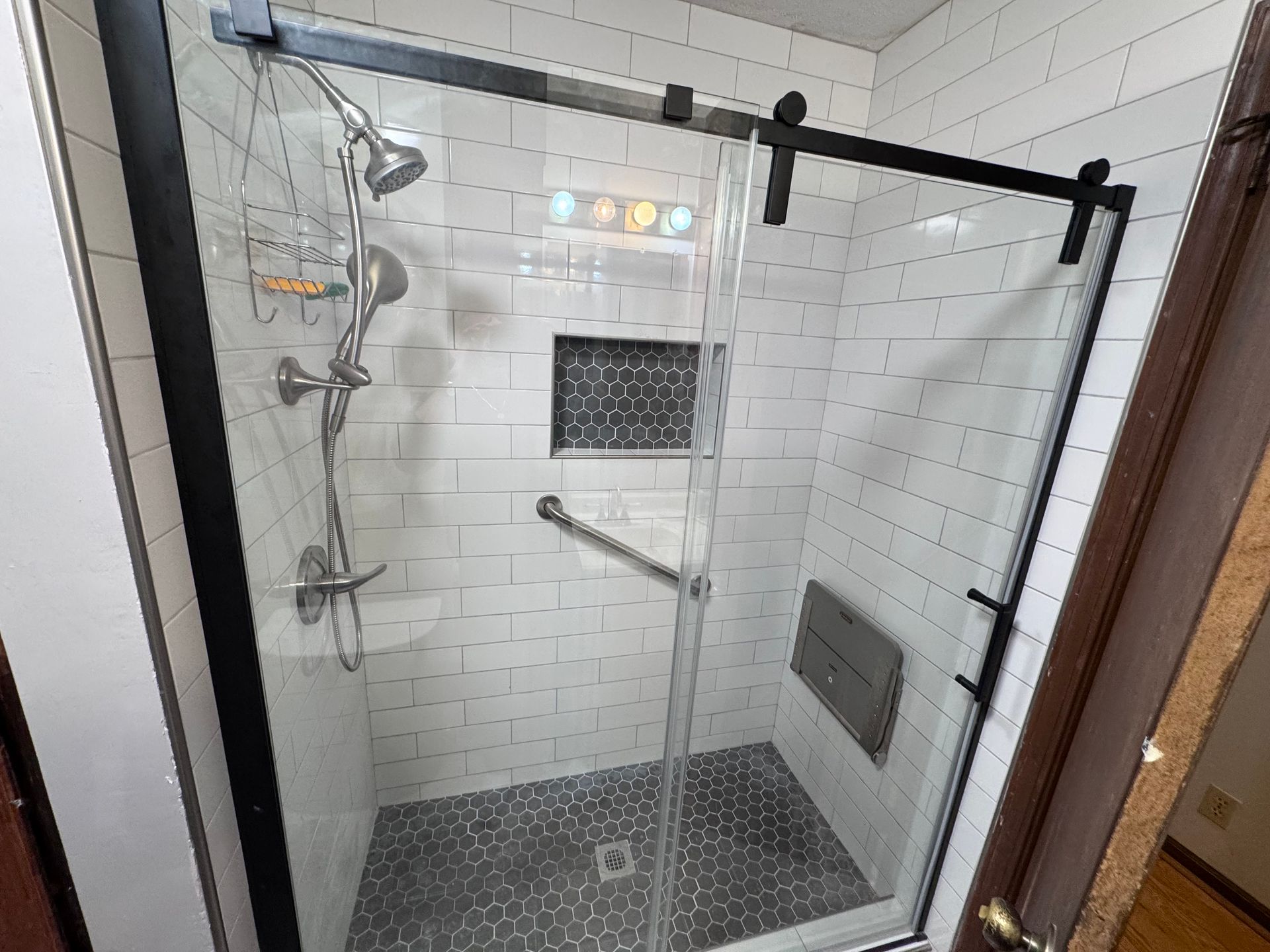 Shower with black frame and sliding glass door, white tile walls, gray tile floor, and chrome fixtures.