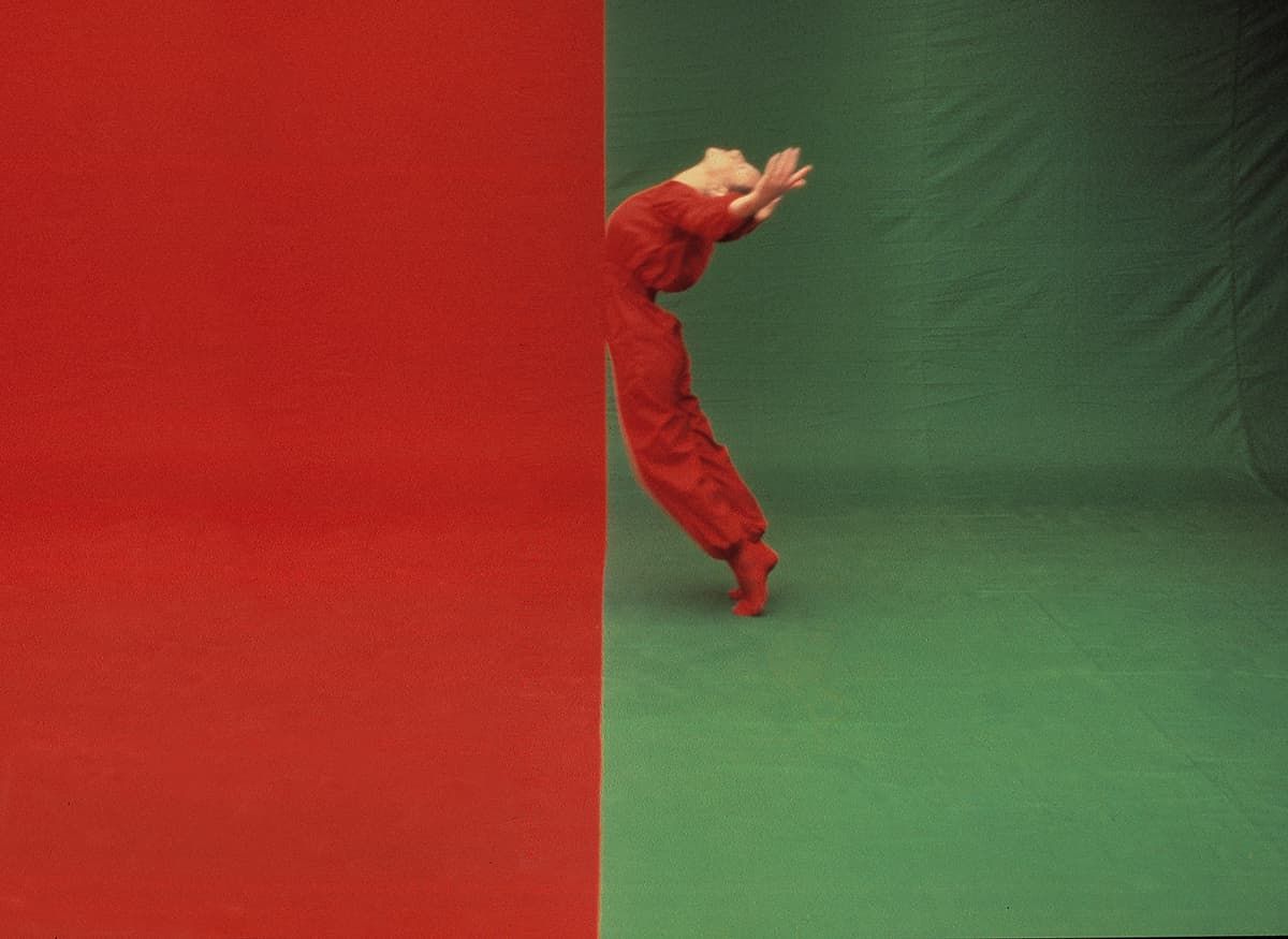 Una persona in tuta rossa balla su uno sfondo verde e rosso.